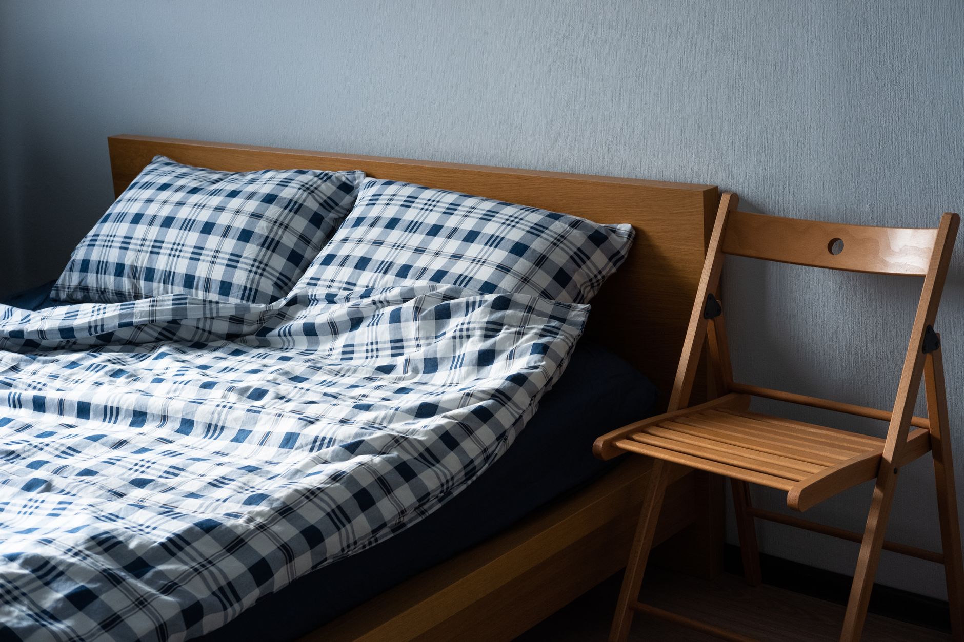 A queen-size Avocado Green Mattress on a simple wood bed frame, photographed under natural window light with a four-foot aluminum straightedge and feeler gauge resting on the corner.
