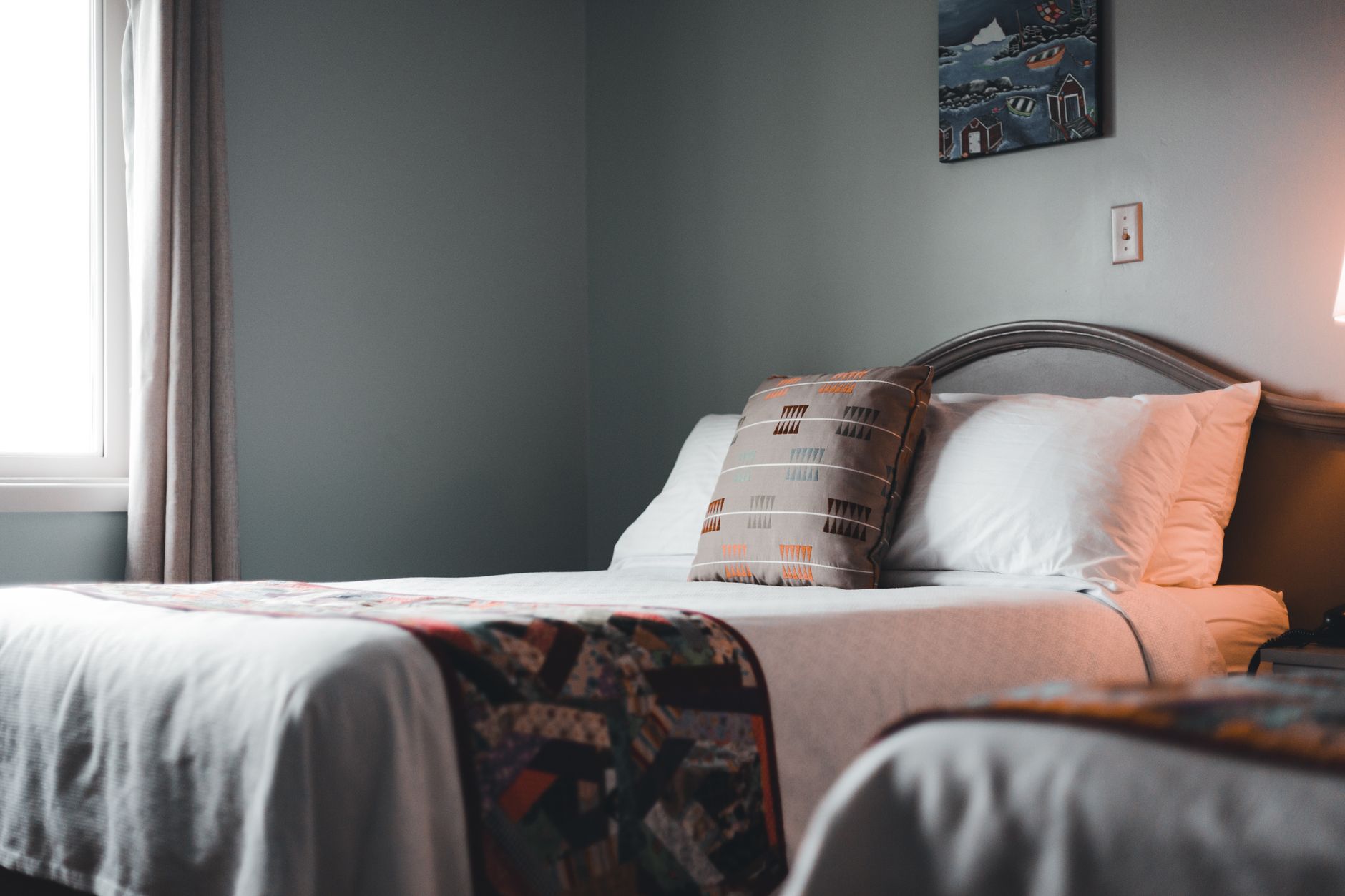 overhead shot of a neatly made bed with a gray upholstered headboard and folded white duvet in soft morning light