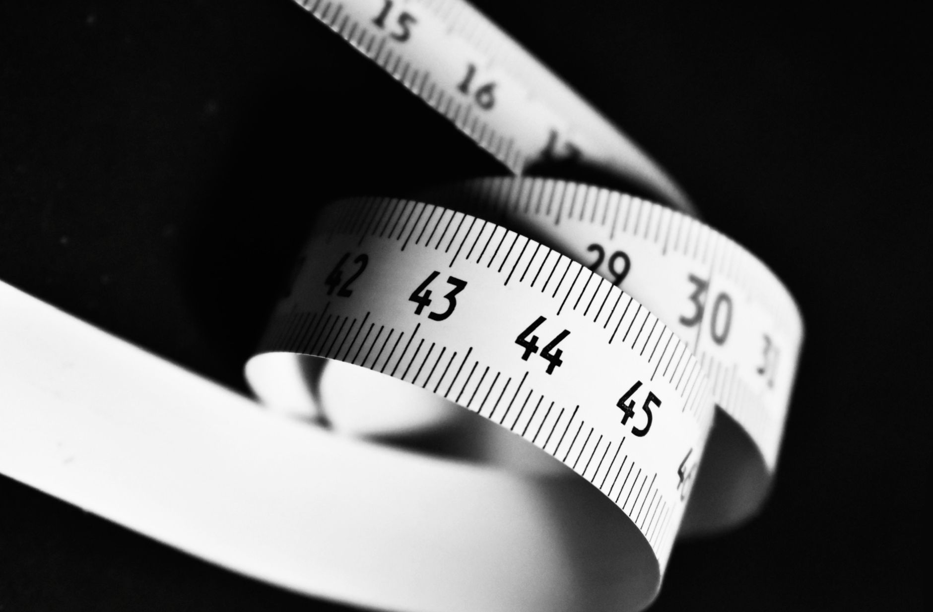 a tailor's tape measuring the inseam of a pair of dark gray boxer briefs laid flat on a wooden table, with a spreadsheet and a digital scale visible in the background.